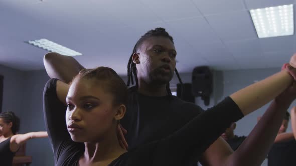 Mixed race fit male modern dancer supporting female dancer while stretching up alt