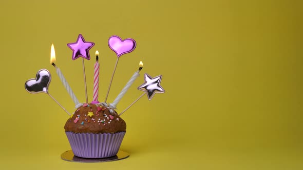 Birthday Cupcake with Candles and Birthday Decorations on Yellow Background alt