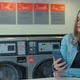 Woman Using Smartphone While Washing Her Laundry at Laundromat - VideoHive Item for Sale