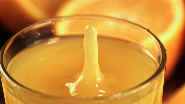 A Drop of Water with Spray Falls Into a Glass of Orange Juice alt
