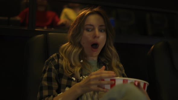 Woman Sitting in Armchair Watching a Horror Movie at the Cinema Scatters the Popcorn From Fear alt