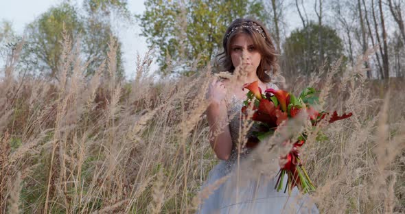 A Young Woman Dressed in a Gray Wedding Dress. She Has Flowers in Her Hand and Is in the Park alt