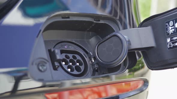 Hand plugging in EV car charger or electric vehicle. Cable connect to gas station alt