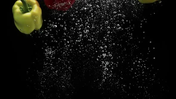 Three Peppers Red and Yellow Falling Into Water and Spinning Air Bubbles Black Background alt
