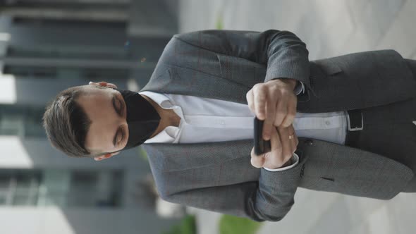 Man Wearing Protective Face Mask Use Smartphone COVID-19 Coronavirus Infection Near Office Building alt