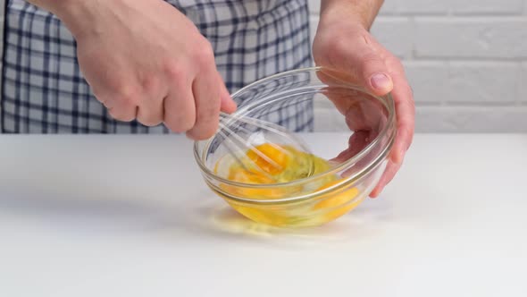 Male hands beat eggs in a glass bowl a whisk.