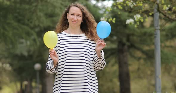 smiling woman with blue and yellow air balloons in hands outdoors. Ukrainian girl in striped 