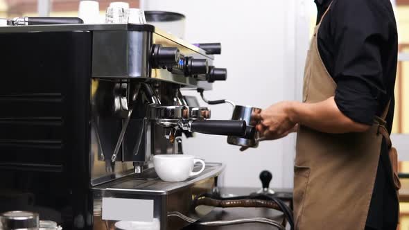 Male barista steaming milk and brewing coffee with machine at cafe