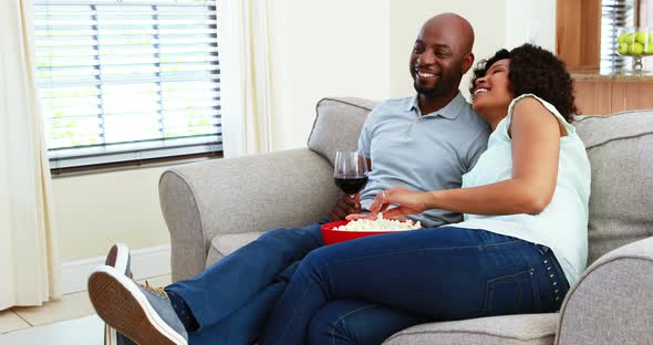 Couple having snacks while watching television in living room 4k alt