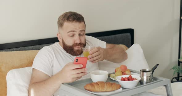 Bearded Young Man Choking on While Drinking Juice and Reading Shocking News, Handsome Guy in Middle