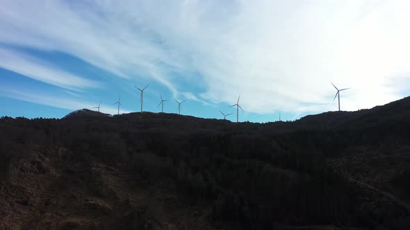 Wind turbines at mountain Midtfjellet in Fitjar Island in Norway - Sidewaysing aerial with dark fore alt