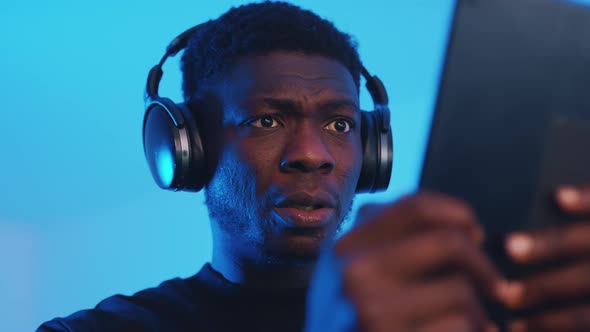 Guy Wearing Headphones and Holding a Tablet Watching Some Video alt