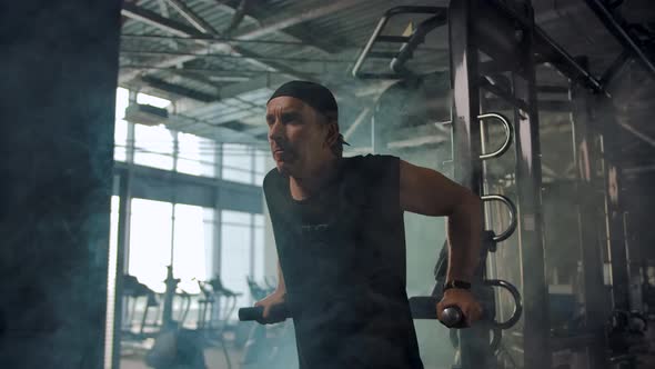 Mature Man in the Gym Doing Back Pushups on the Simulator with Parallel Bars alt