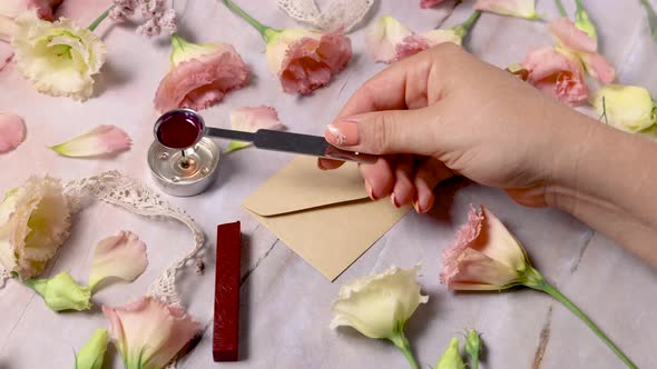 Hands pouring melted wax and sealing an envelope near pink flowers alt