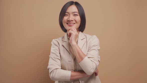 Happy business asian woman have a good idea crossed arms standing isolated over beige background.