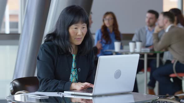 Mature Asian businesswoman using laptop computer in office lobby