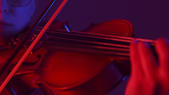 Woman Musician Plays on Strings of the Violin with Bow a Closeup in the Red Light of Studio alt