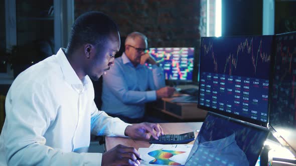African Stockbroker is Doing Calculations at His Desk alt