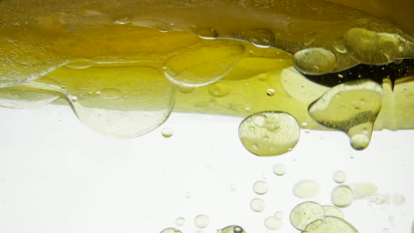 Mixing Linseed and Sesame Oil on a White Background. Pouring Golden Liquid with Water Into a Glass alt