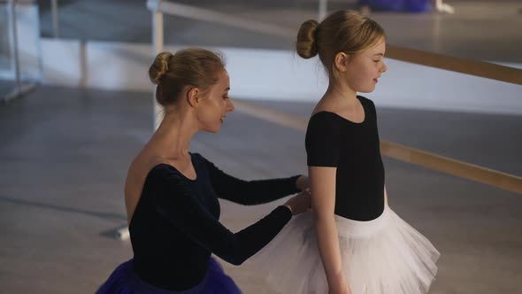 Confident Gorgeous Slim Woman Adjusting Tutu of Cute Smiling Girl and Hugging Child alt