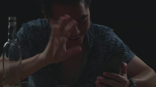 Asian Man Pouring Vodka In A Shot Glass Before Drinking During Having Video Call In Black Background alt