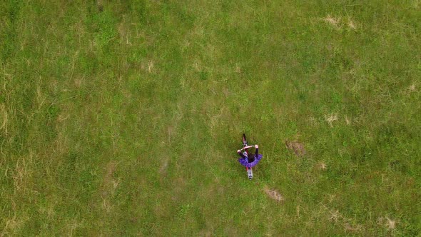 A Beautiful Little Girl Rides a Kids Bicycle Across the Field View From Above Aerial View alt