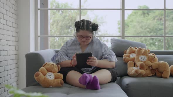 young Asian girl with Down's syndrome is playing a tablet alone in the room alt