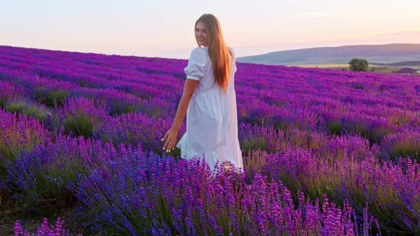 Young Woman in White Dress Walking Through a Lavender Field on Sunset