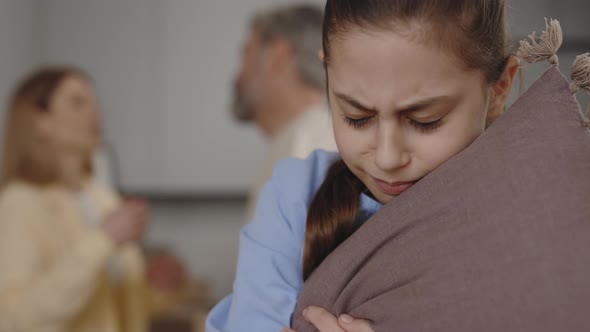 Close View of the Sad Little Girl Holding the Pillow Listening Her Parents Arguing on Background alt