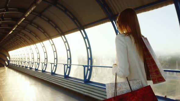 Successful Woman with Shopping Bags Walks Through a Glass Tunnel, the Sun Beautifully Illuminates alt