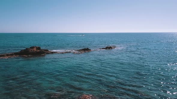 Flying over the Mediterranean coast offshore, a motor boat crosses the horizon of the sea