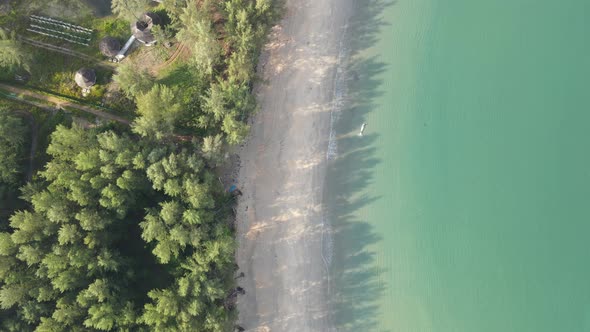 Top down aerial view and fly over beach near resort or village with green color of water