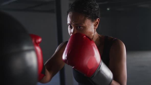 African american woman wearing boxing gloves training in empty building punching punchbag alt