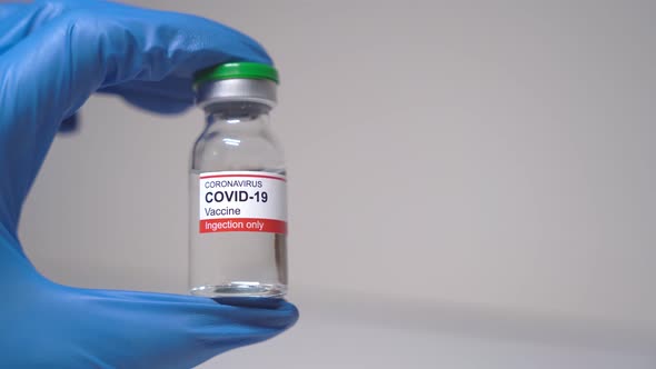 A hand in a blue medical glove holds a glass bottle of liquid.