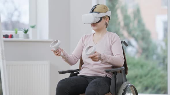 Active Young Paraplegic Woman Using Virtual Reality Headset Sitting on Wheelchair Indoors alt