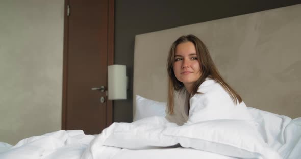 Positive Lady Rests Sitting on Comfortable Bed in Hotel Room