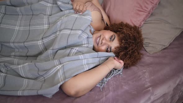 Beautiful Curvy Plus Size African Black Woman Afro Hair Lying on Bed with Grey Plaid Blanket Cozy