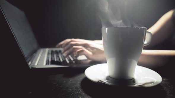 Typing on a laptop keyboard, with a cup of coffee