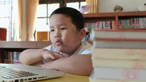 Little asian boy studying online from home watching web class lesson or listening tutor by video cal alt