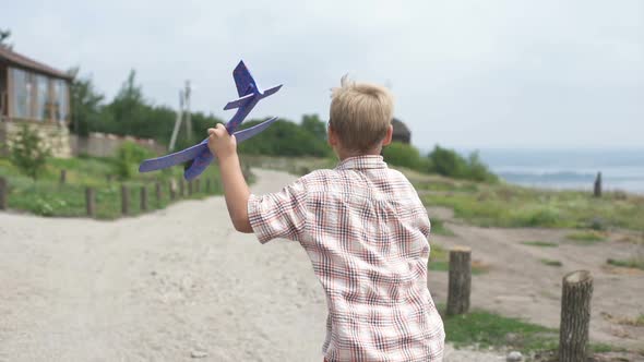 A Boy with an Airplane in His Hands Runs in the Park