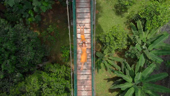 Aerial Shot of a Young Woman and Her Little Son Laying on a Suspension Bridge Over the Jungles alt