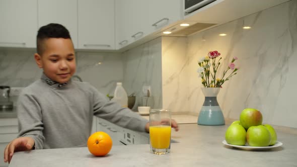 Cheerful Black Boy Choosing Between Orange and Glass of Juice Indoors alt