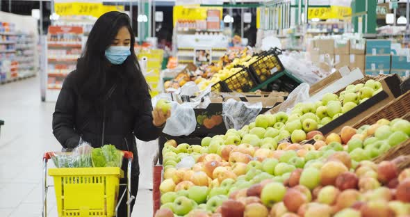 Woman Buys Fruits in Supermarket with Protective Face Mask Puts Apple in Basket