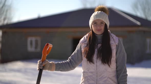 Young Girl Stands with a Shovel in the Backyard. Woman Ready To Clear Snow After Snowfall alt