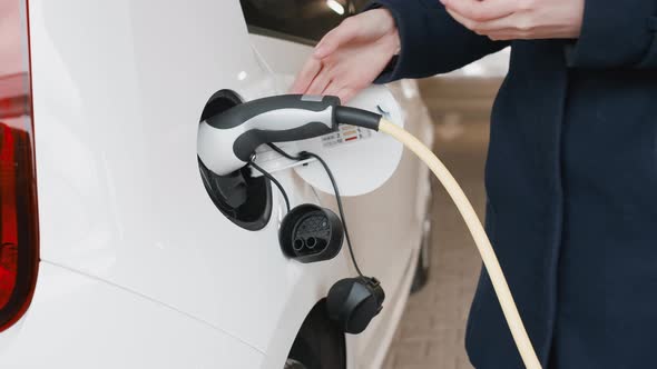 Womans Hand Unplugging an Electric Car After Charging in the Parking alt