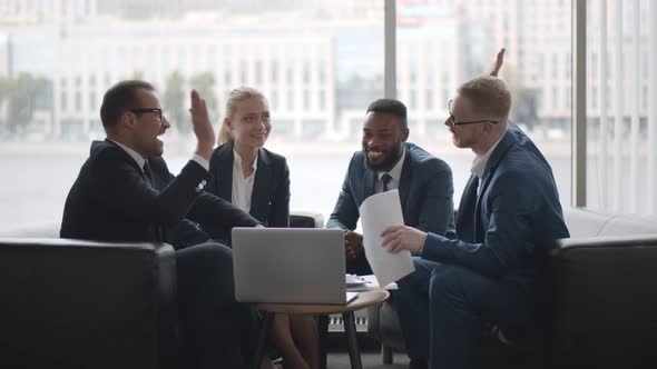 Team of Successful Entrepreneurs Sharing High-five Celebrating Success Sitting on Couch in Office alt