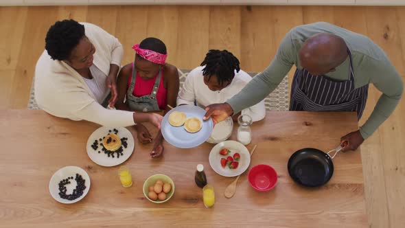 Overhead view of african american grandparents and grandchildren preparing pancakes in the kitchen alt