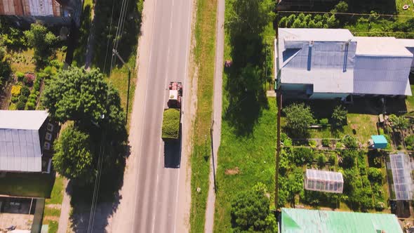 An Agricultural Tractor Pulls a Full Cart with Mowed Green Grass Aerial View alt