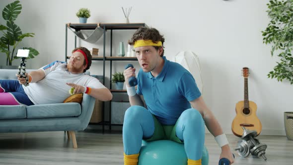 Guy Training with Dumbbells and Fitball While Friend Vlogger Recording Video Eating Apple Showing alt