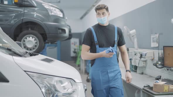 Young Confident Auto Mechanic in Covid Face Mask Walking in Auto Repair Shop To Tools Set alt
